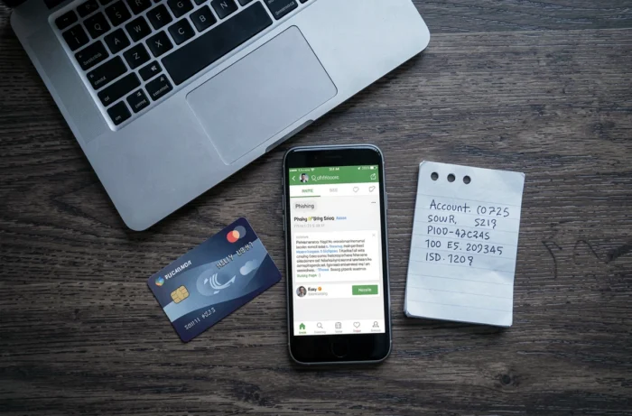 Vue en plongée d'un bureau avec carte bancaire, ordinateur portable et téléphone affichant un email de phishing bancaire